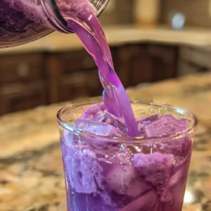Pouring blended purple peel drink into a clear glass over ice