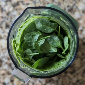 Blender in action blending green smoothie with ingredients nearby