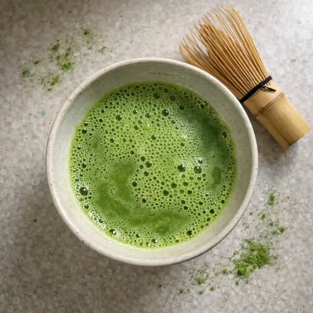 Freshly whisked matcha tea in a bowl with bamboo whisk and foamy surface