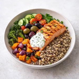 Healthy Mediterranean grain bowl with salmon, quinoa, roasted vegetables, olives, and yogurt sauce on ceramic plate